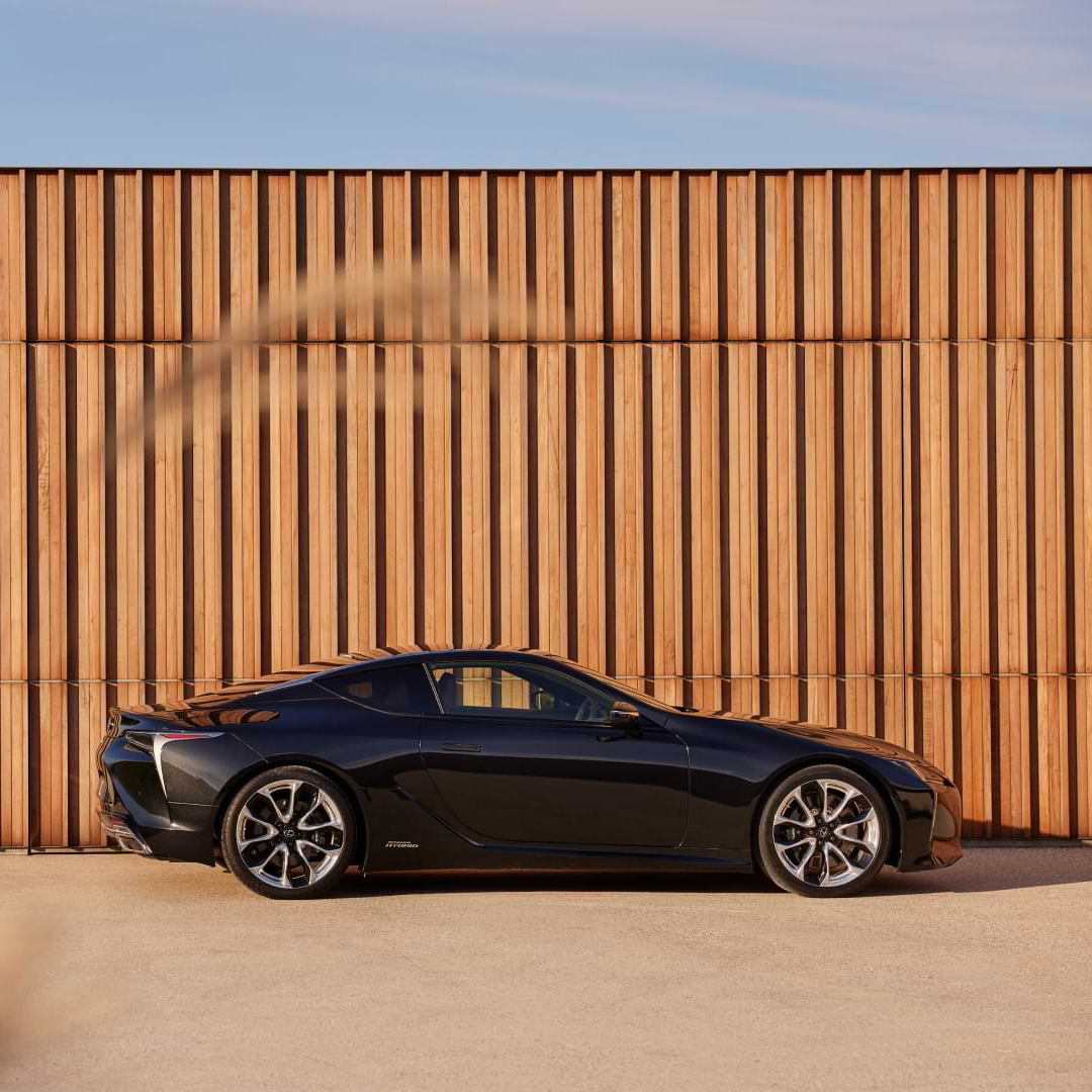 Lexus LC Hybrid parked on gravel in front of a timber slat wall.