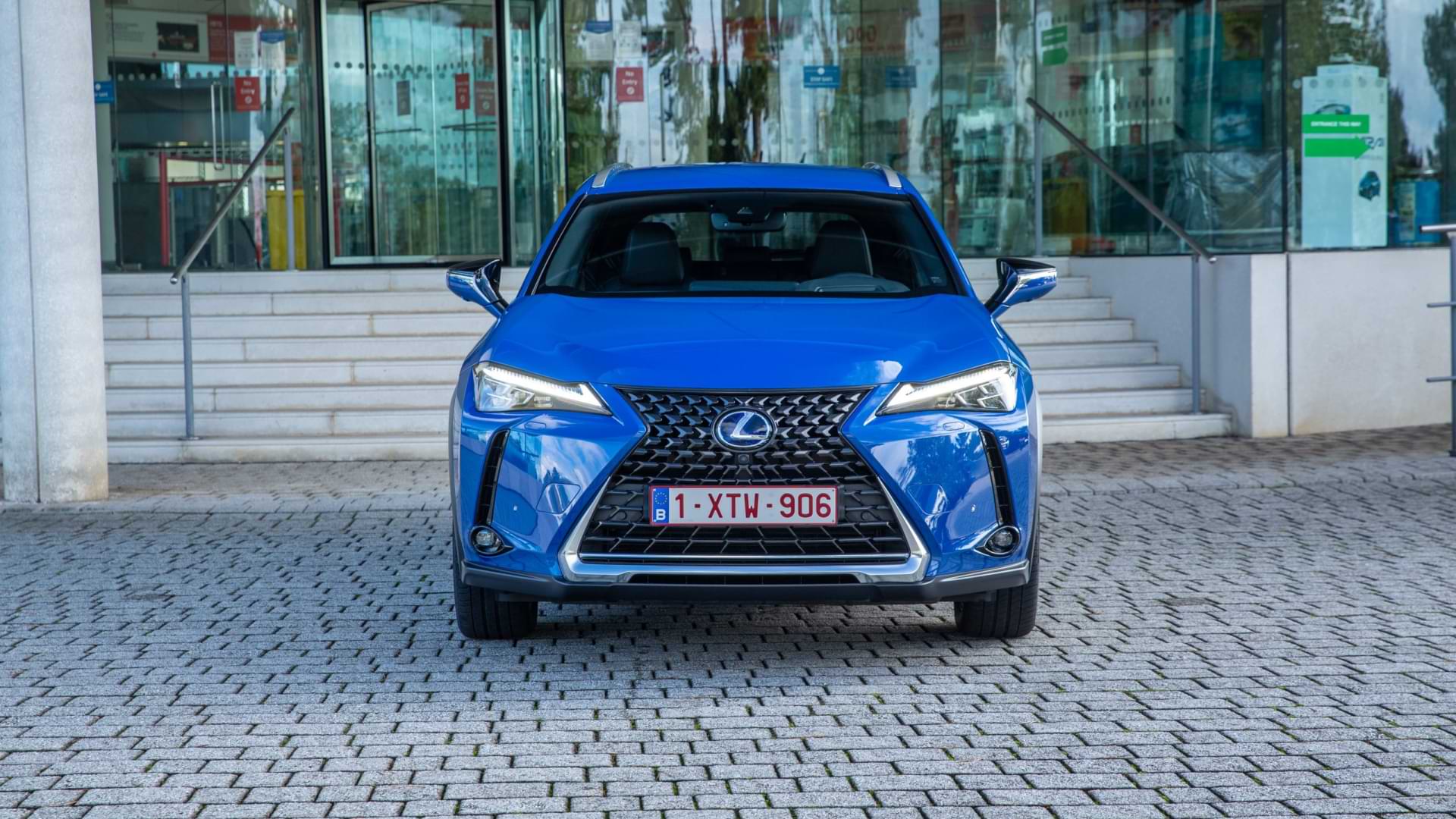 A blue UX 300e with its headlamps lit sits parked on cobblestones.