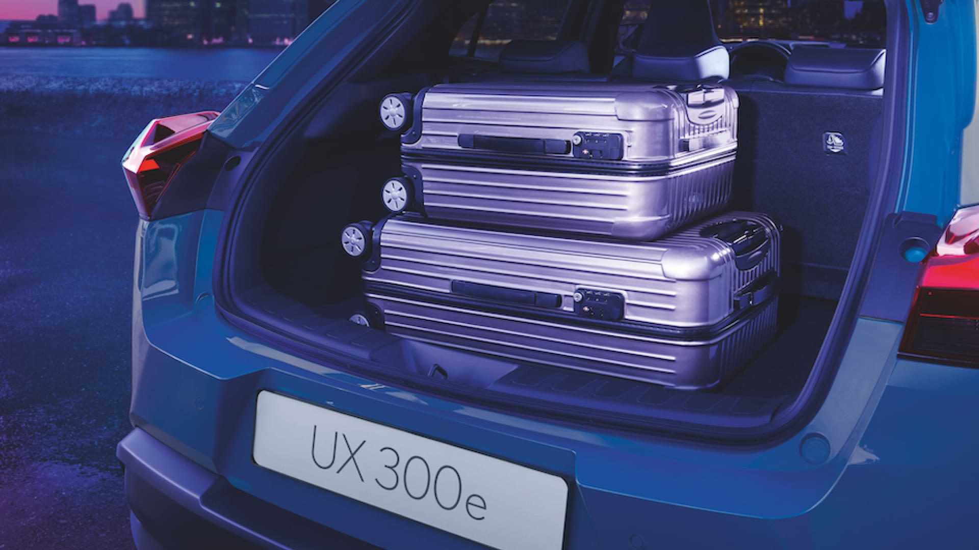 Two suitcases stacked on each other appear in the open boot of the UX 300e.