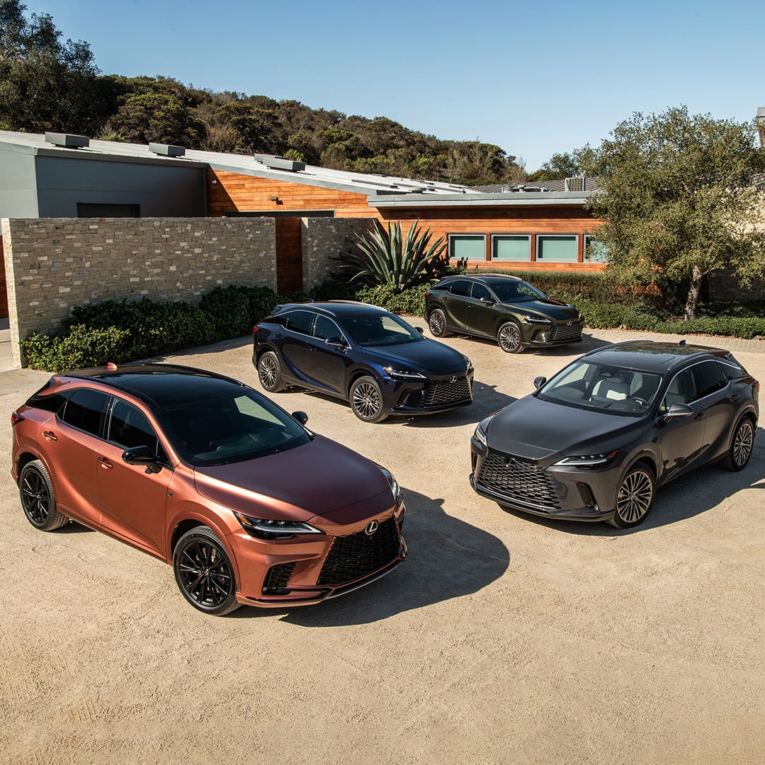 Four differently coloured Lexus RX models parked in the driveway of a contemporary luxury home.